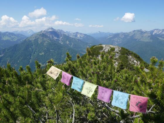 Gebetsfahnen wehen im Wind; Gipfelblick nach Westen in Richtung Guffert, Hinteres Sonnwendjoch, Risserkogel und Rotwand