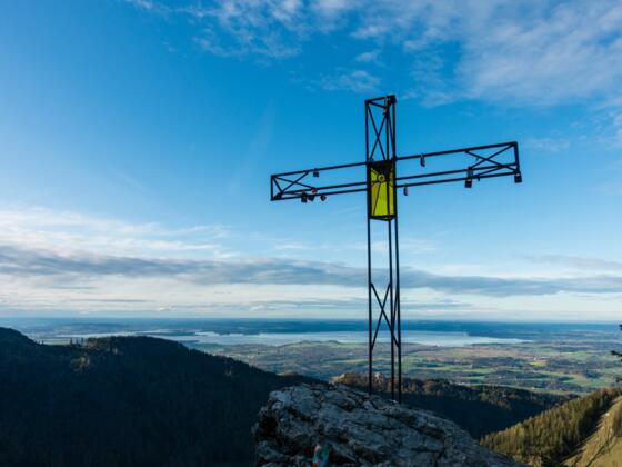Gipfelkreuz am spitzen Stein mit farbigen Glas über dem Chiemsee.
