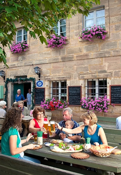 Bei der Brotzeit im Biergarten der Fuchsmühle bei Hilpoltstein stoßen Gäste mit kühlem Bier an und genießen die Köstlichkeiten.