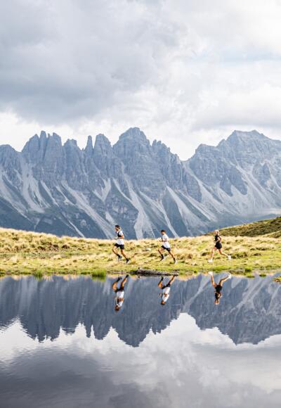 Drei Trailrunner:innen laufen vor dem Salfeiner See