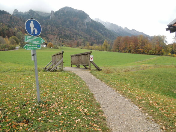 Brücke hinter einer Hofstelle mit Wegweiser zur Kampenwandseilbahn