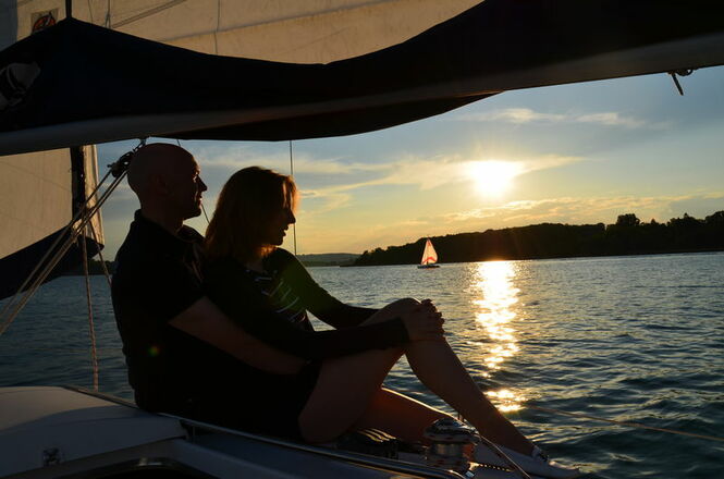 Segler beobachten den Sonnenuntergang am Chiemsee vom Schiff aus.