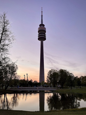 Sicht auf den Olympiaturm mit dem Olympiasee im Vordergrund bei Sonnenuntergang