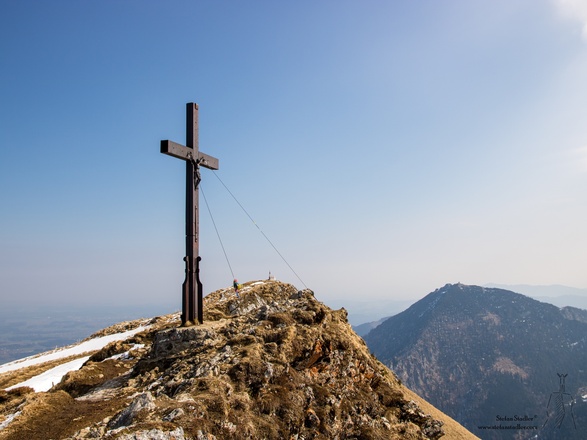 Gipfelkreuz des Hochgern mit dem Hochfelln im Hintergrund.