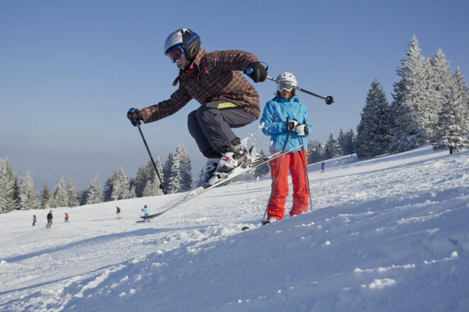 Mädchen in Skiausrüstung springt über eine Sprungschanze.