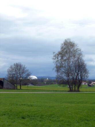 Blick vom Weg auf die große weiße Kugel des Industriedenkmals Radom Raisting auf dem Areal der Erdfunkstelle - dahinter die Alpen.