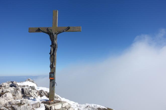 Hinter dem Hochthron-Gipfelkreuz wogt das Nebelmeer der Südwand.