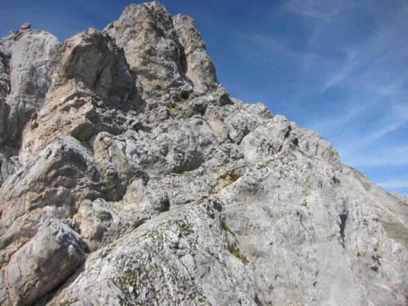 Der erste mächtige Steilaufschwung. Wir traversieren auf der Rampe ganz nach rechts (Anseilpunkt.) Rechts oben ist der Kamin gut sichtbar. In diesem Kamin empor (1. SL).