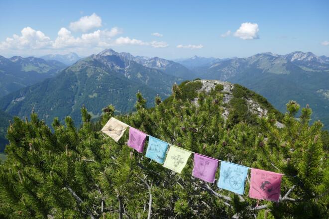 Gebetsfahnen wehen im Wind; Gipfelblick nach Westen in Richtung Guffert, Hinteres Sonnwendjoch, Risserkogel und Rotwand