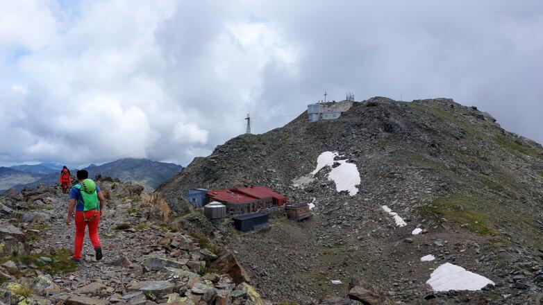 Die Glungezer Hütte des Alpenverein Hall in Tirol. Darüber der Glungezer-Gipfel mit Gipfelkreuz und Anlage zur militärischen Luftraumüberwachung.