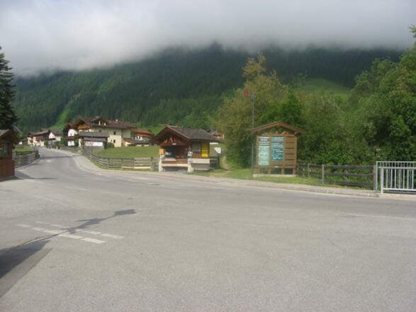 Wir erreichen die Straße nach Milders und folgen der Forststraße zwischen Bushaltestelle und Infotafel.