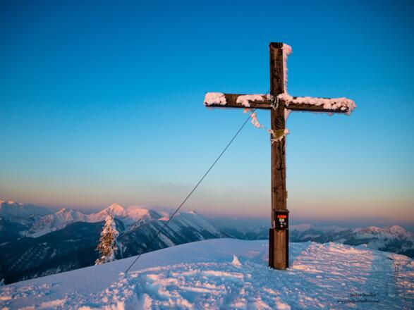 Gipfelkreuz Hochplatte und der Geigelstein im ersten Sonnenlicht.