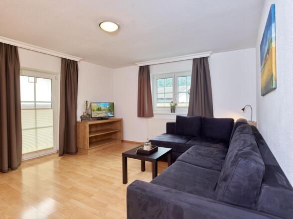 Wohnzimmer mit Eckcouch und Zugang zum Balkon