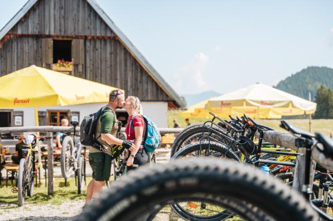 zwei Radfahrer die sich auf der Ebenforstalm im Hintergrund küssen.