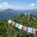 Gebetsfahnen wehen im Wind; Gipfelblick nach Westen in Richtung Guffert, Hinteres Sonnwendjoch, Risserkogel und Rotwand