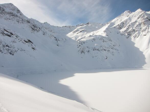 Das Südende des Stausees. Durch das Tal in Bildmitte in Richtung der Licht-Schatten-Grenze verläuft der weitere Anstieg.