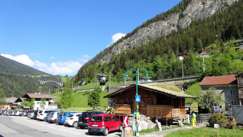 Parkplatz im Ortskern. Hinten die Bahnhaltestelle und die Bahnunterführung. Oben die Stafflacherwand (Klettersteig).
