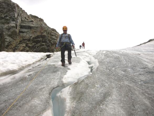 Knapp links (im Sinne des Abstiegs) des Felskopfs in der Flanke weiter nach unten (knapp 40°, steilstes Teilstück des Abstiegs). Die Instruktoren im Bild wählten hier als Sicherungsmethode ein Geländerseil (Fixseil).